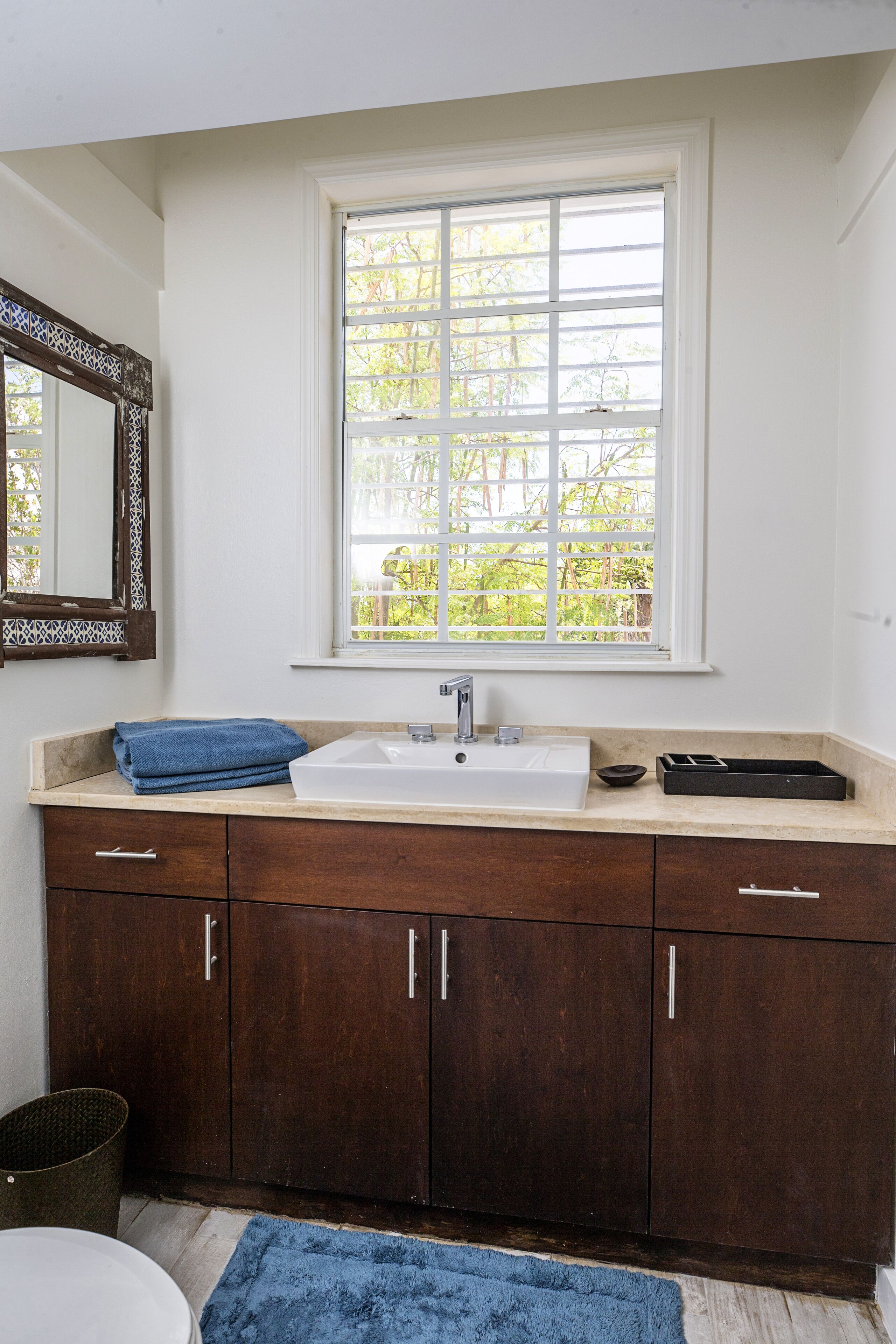 A bathroom with a white sink, dark wooden cabinets, a blue towel, and a window with a view of greenery.