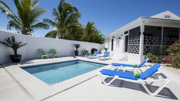A swimming pool with lounge chairs, a covered area, and palm trees.