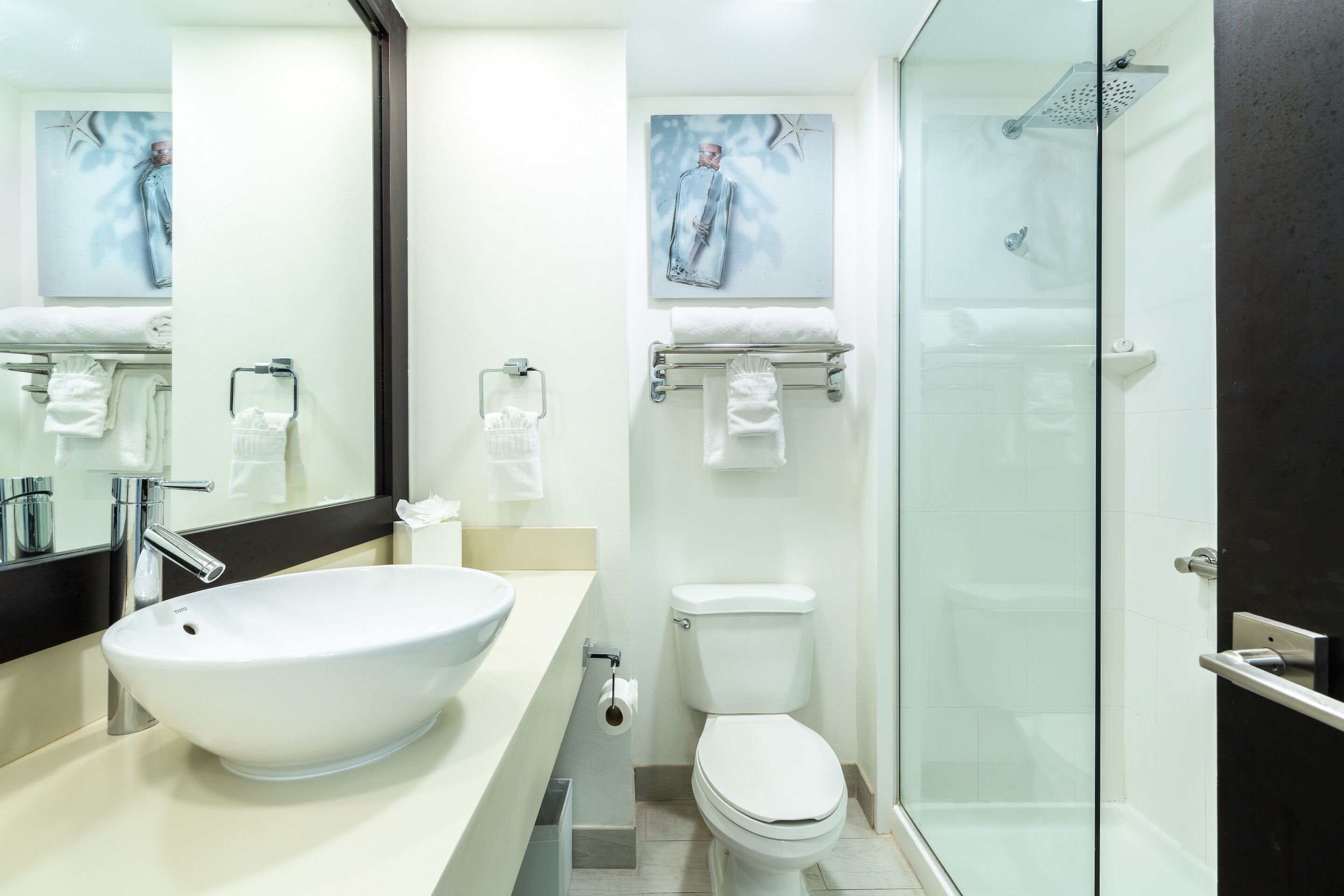Un baño moderno con un lavamanos blanco grande, un inodoro y una ducha con cerramiento de vidrio.