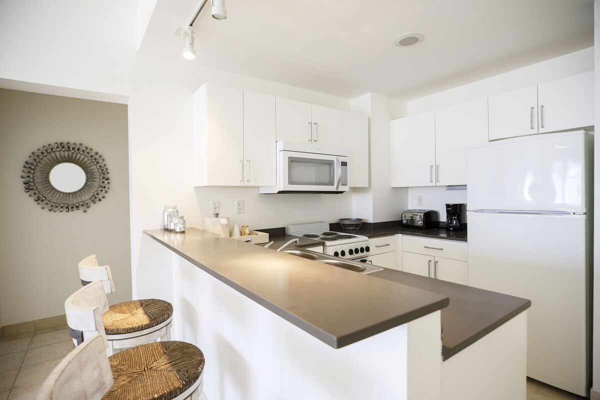 Een moderne keuken met witte kasten, een roestvrijstalen eiland, een magnetron, een fornuis en een koelkast.