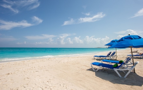 A beach with white sand, clear turquoise water, and blue umbrellas providing shade.