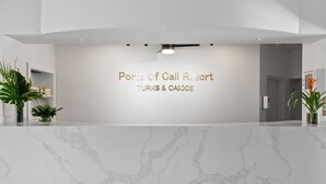 A reception area with a marble counter, a sign reading "Ports Of Call Resort TURKS & CAICOS," and potted plants on either side. - Ports of Call Resort Turks, Tapestry Collection by Hilton (Providenciales)