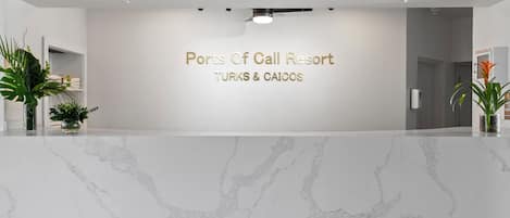 A reception area with a marble counter, a sign reading "Ports Of Call Resort TURKS & CAICOS," and potted plants on either side.