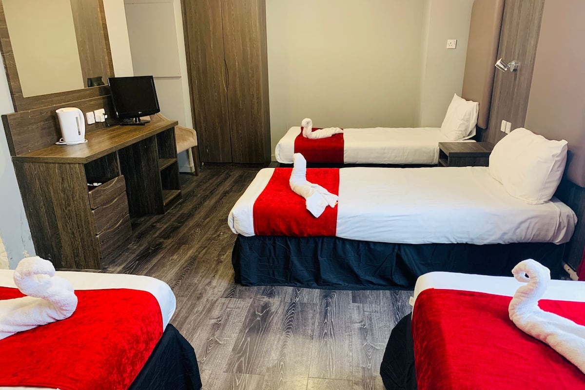 A hotel room with two beds, each with a red and white bedspread, a wooden desk with a computer and a coffee maker, and a wardrobe.