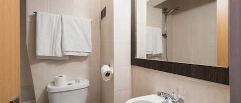 A bathroom with a toilet, two rolls of toilet paper, a sink with a mirror above it, and a towel rack with two towels.