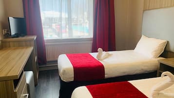 A hotel room with two beds, a desk, a television, and a window with curtains.