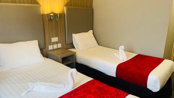 Habitación de hotel con dos camas, cada una con sábanas blancas y almohadones rojos. Cuenta con luces fijadas a la pared y un cabecero de madera.
