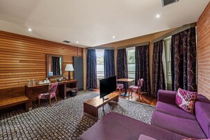 Una sala de estar moderna con una pared de madera, un sofá, un televisor sobre un mueble bajo, un escritorio con una silla y una alfombra estampada.