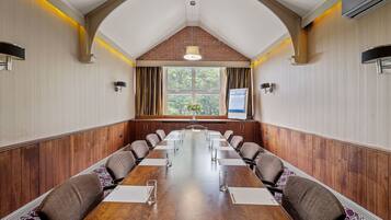A conference room with a long wooden table, multiple chairs, and a large window with curtains.