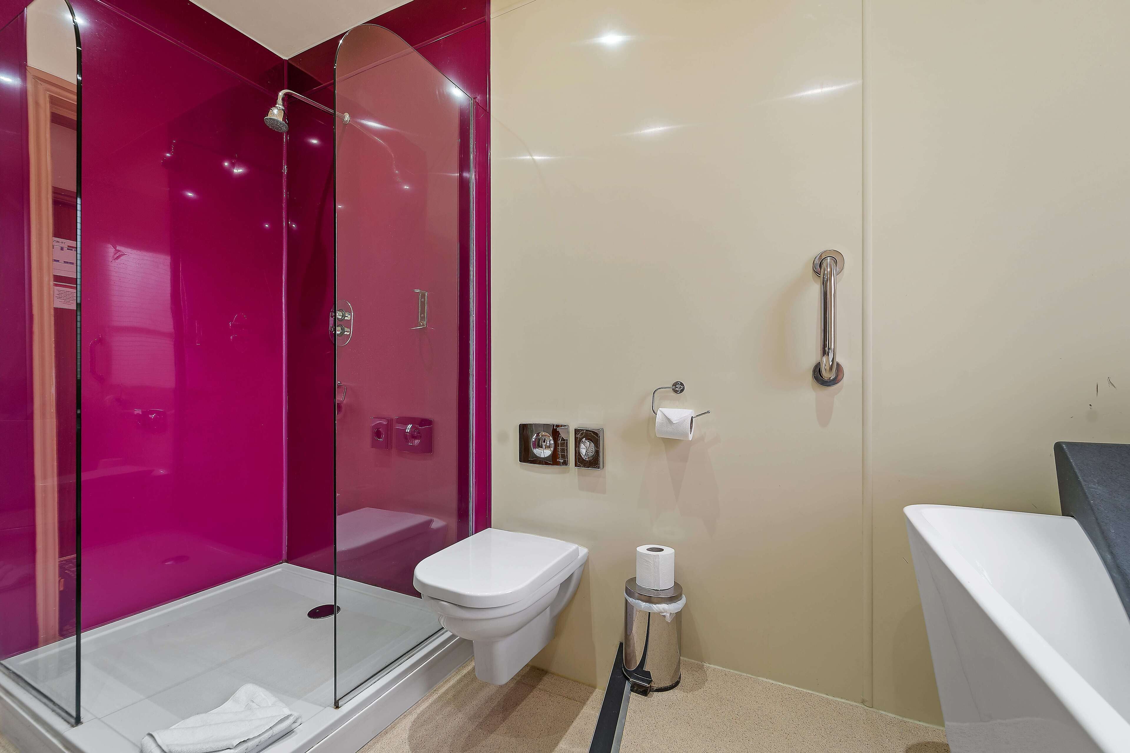 Une salle de bain avec une douche à parois de verre, des toilettes blanches et une poubelle.