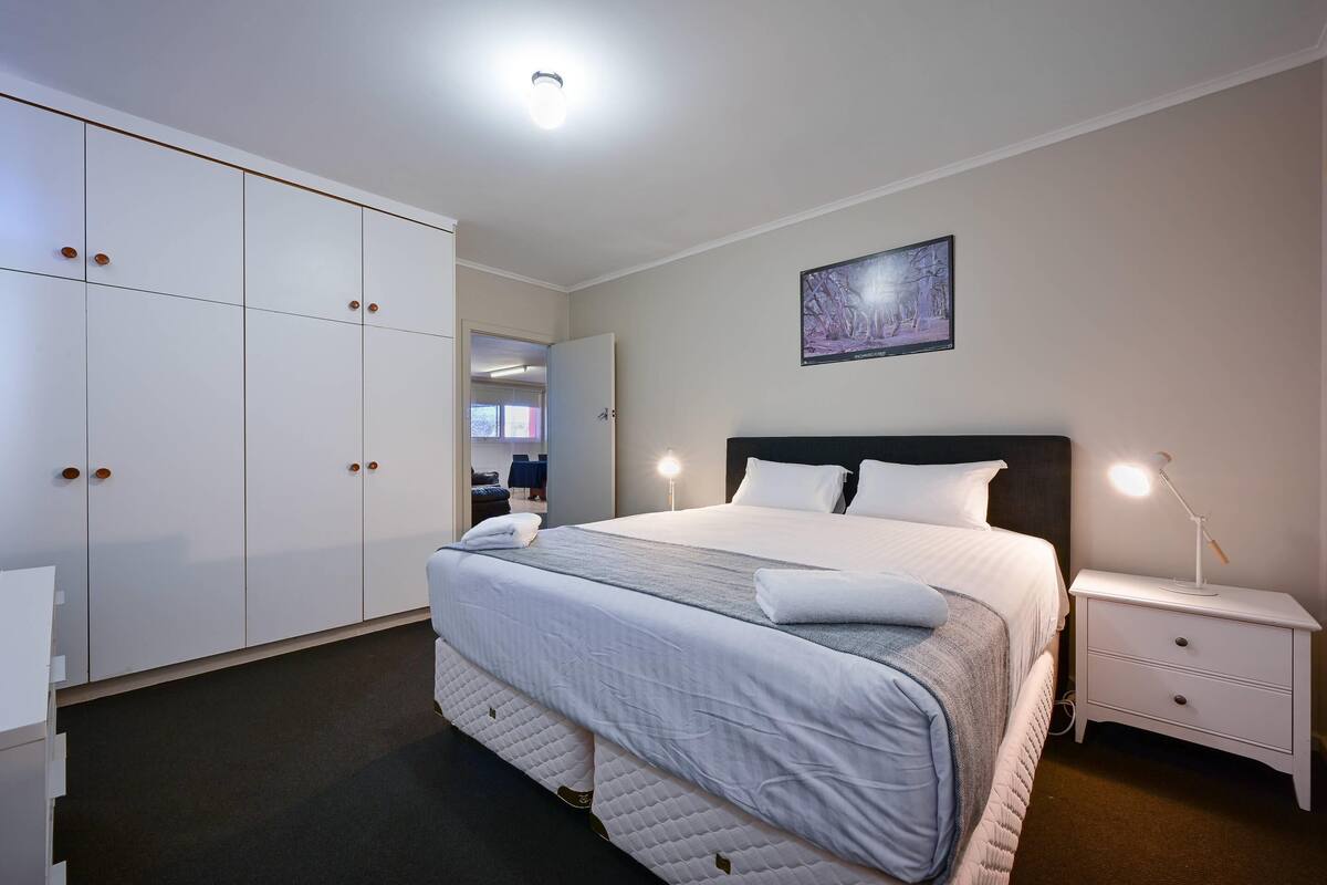 A bedroom with a large bed, a nightstand, a wardrobe, and a painting on the wall.