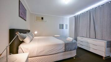 A modern hotel room with a large bed, bedside lamp, and a dresser with drawers.