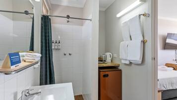 A hotel bathroom with a shower, a sink, and a toilet. There is a towel rack with towels, a small cabinet, and a sign indicating the room's amenities.