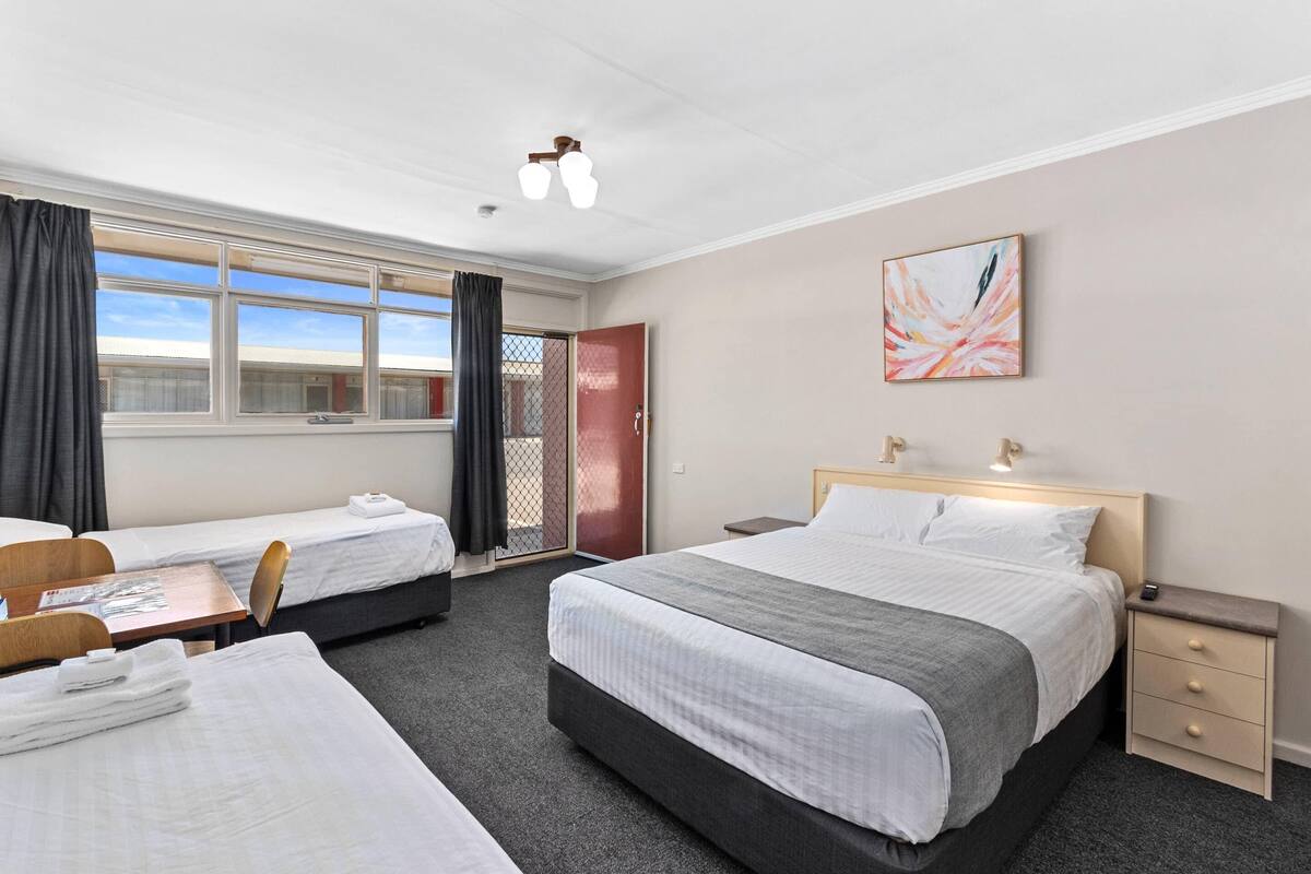 A hotel room with two beds, a desk, a chair, a nightstand, and a window with curtains.