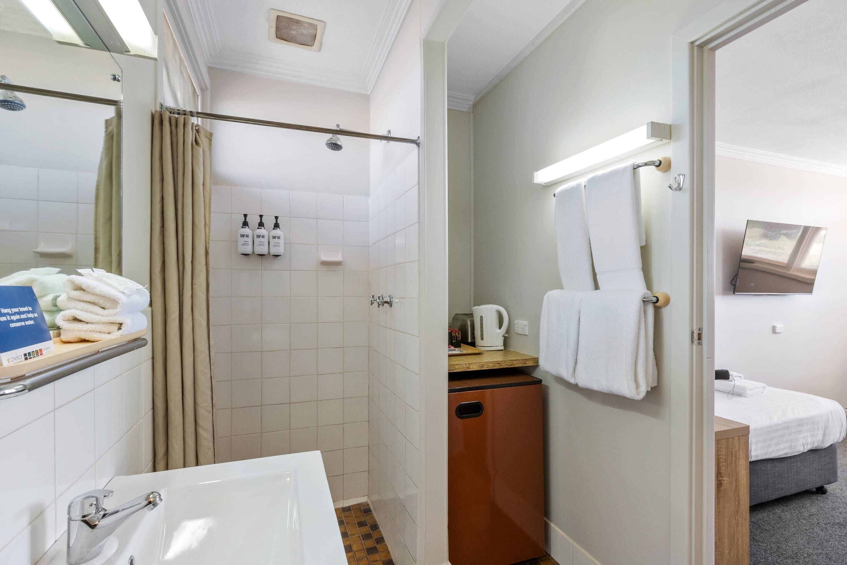 Un baño de hotel con ducha, lavabo y una mesita de noche con una tetera.