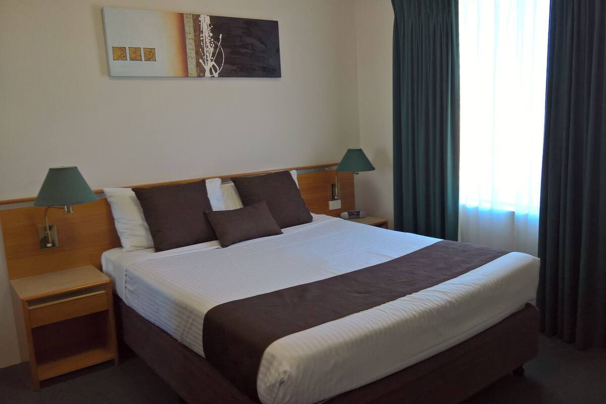 A hotel room with a large bed, two bedside tables with lamps, a headboard, and a painting on the wall.