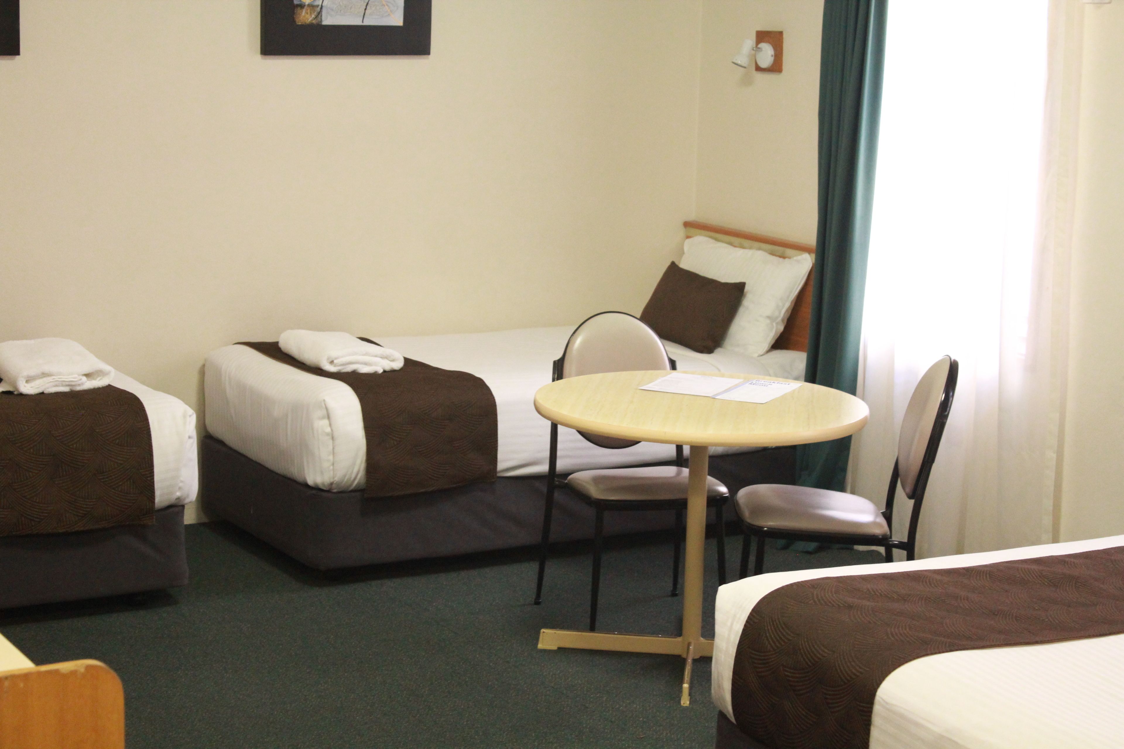 A hotel room with two single beds, a round table, two chairs, and a small desk.