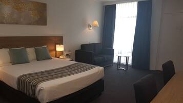 A hotel room with a large bed, a desk, a chair, a lamp, and a window with curtains.