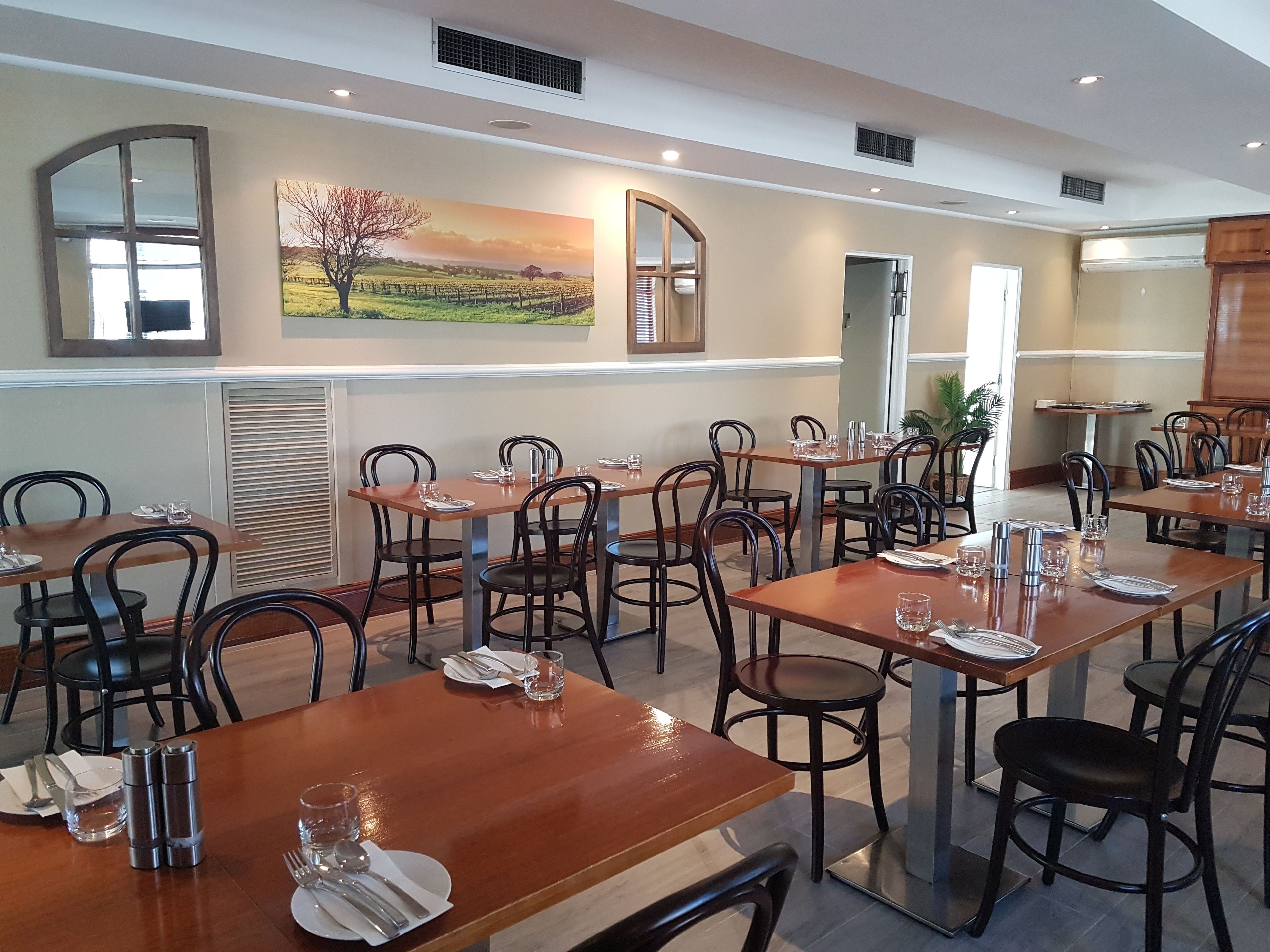 Un restaurant avec plusieurs tables et chaises, un tableau accroché au mur et une fenêtre avec des stores.