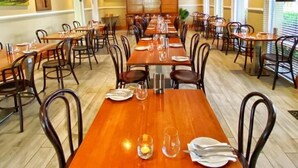 A spacious dining area with multiple tables and chairs, high ceilings, and large windows. - Mid City Motor Inn (Singleton)