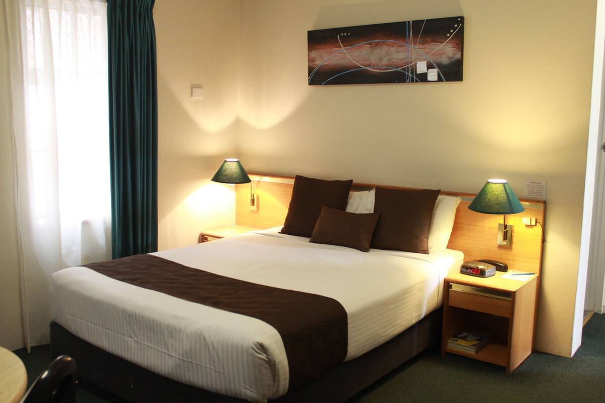 A hotel room with a large bed, two bedside lamps, a nightstand, and a wall-mounted abstract painting.