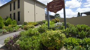 A sign for "The Terrace" serviced apartments with a beige building and a well-maintained garden in front. - Mid City Motor Inn (Singleton)