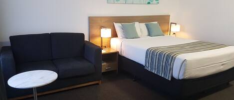 A hotel room with a bed, a sofa, a small round table, and a painting on the wall.