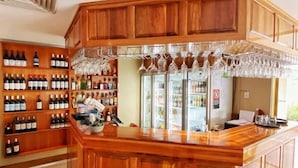 A bar area with wooden cabinets, shelves of wine bottles, and a counter with a glass rack. - Mid City Motor Inn (Singleton)