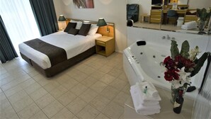 A hotel room with a bed, a bathroom with a bathtub, a desk, and a chair. - Mid City Motor Inn (Singleton)