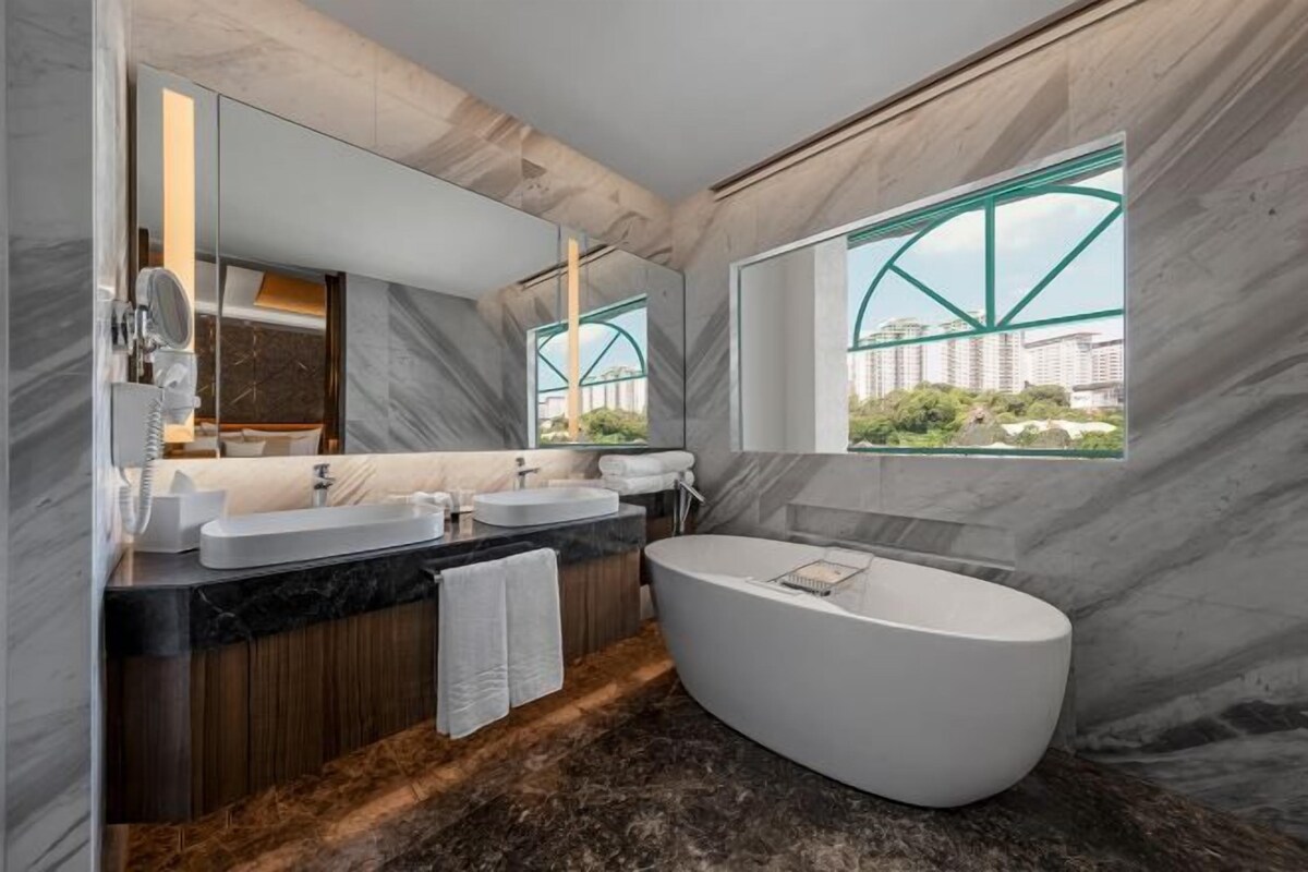 Un baño moderno con dos lavamanos, una bañera grande y vistas a un puente a través de una ventana.