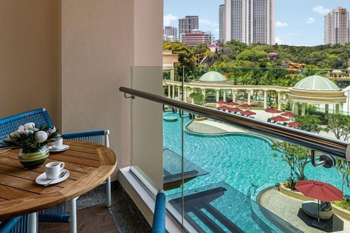 Un balcón con vista a una piscina, una mesa con un florero y una taza, y una barandilla.