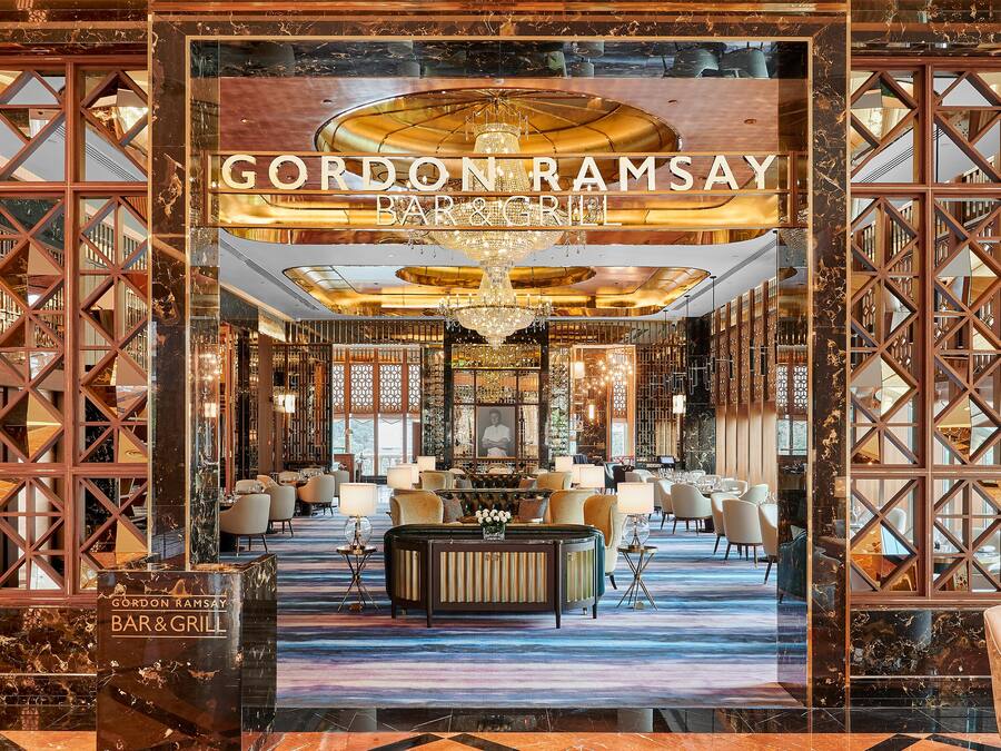 Un interior lujoso del Gordon Ramsay Bar & Grill, con suelos de mármol, muebles elegantes y una araña.