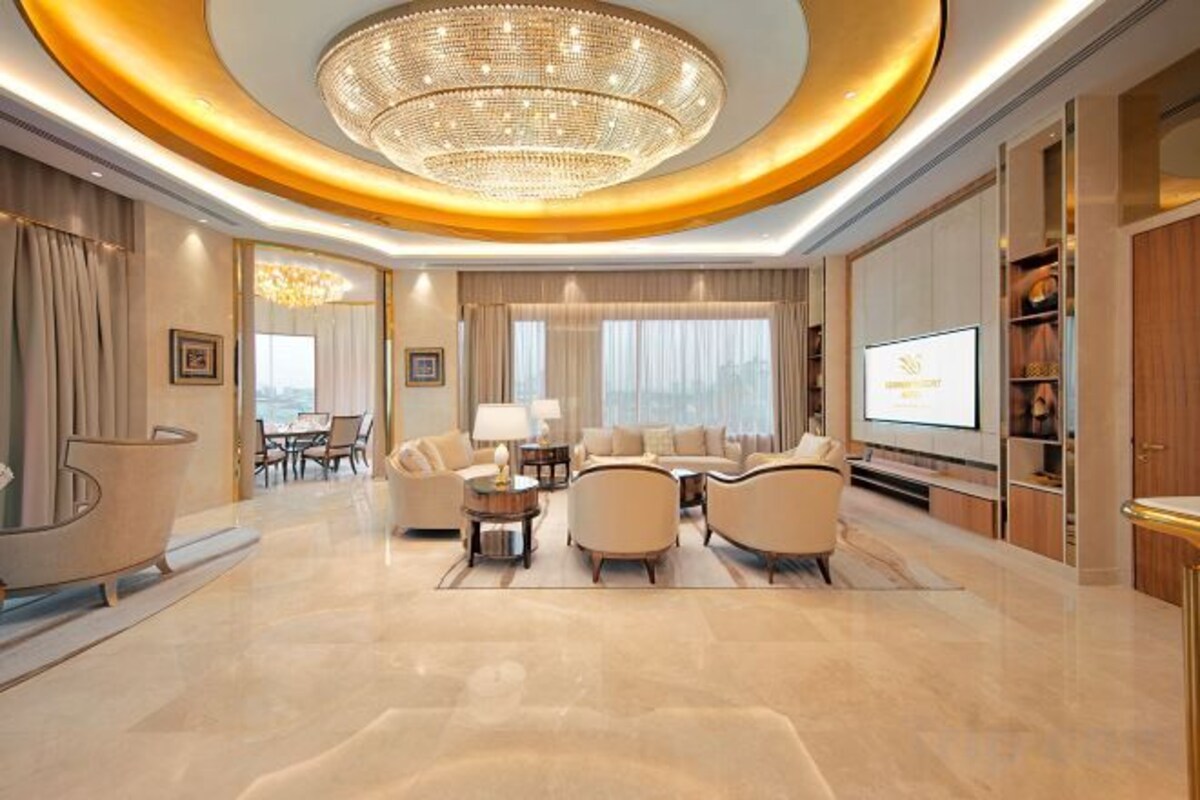 A spacious living room with a large chandelier, comfortable seating, a television, and a view through the window.