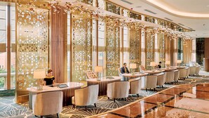 Un vestíbulo de hotel con un mostrador de recepción alargado, varias zonas de estar y paneles decorativos.