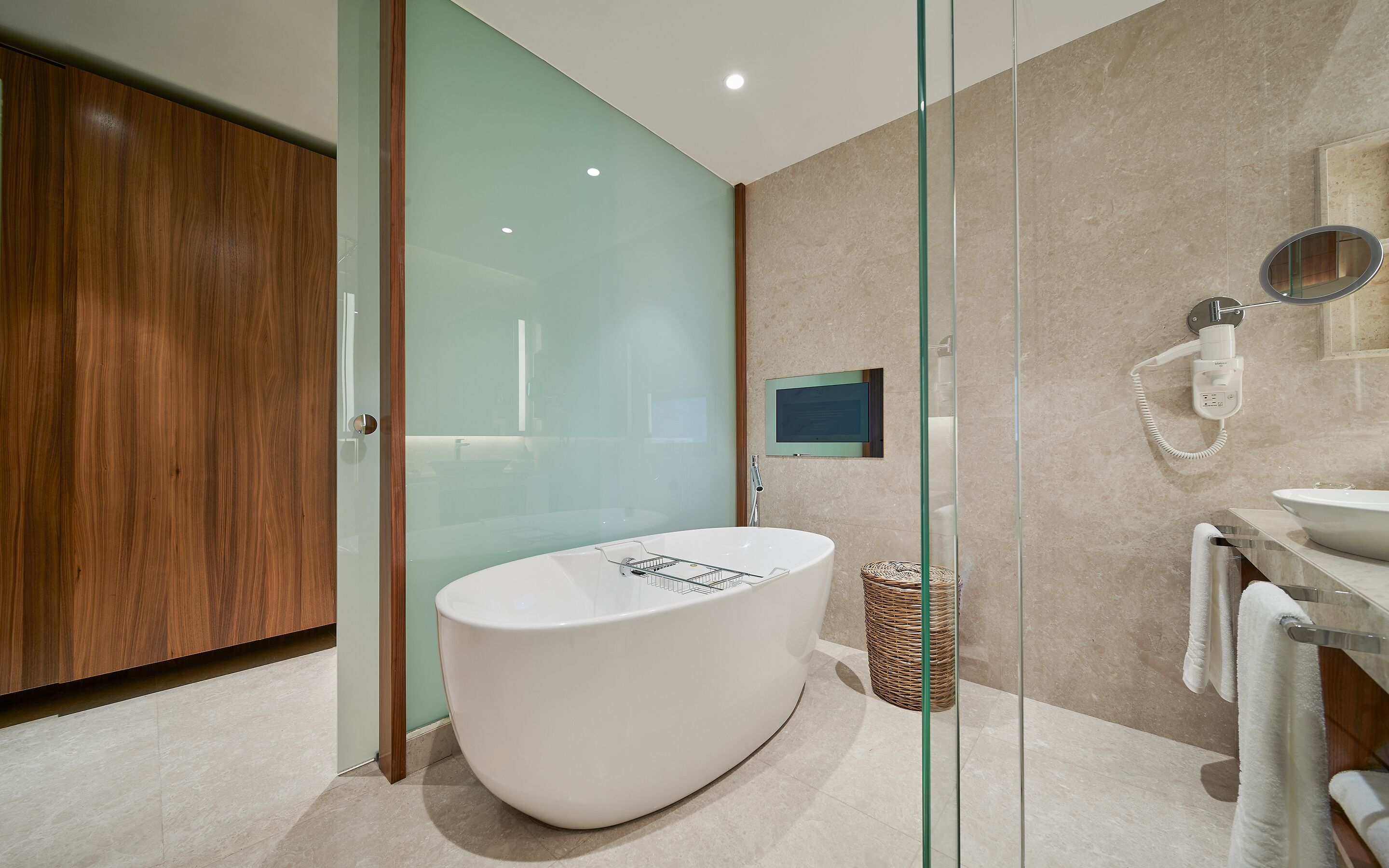 A modern bathroom with a freestanding bathtub, a glass shower enclosure, a mounted TV, and a towel rack.