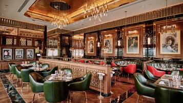 A restaurant with a bar area, green upholstered chairs, and a wooden floor.