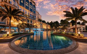 Un hotel con una amplia piscina exterior rodeada de palmeras y un cielo al atardecer.