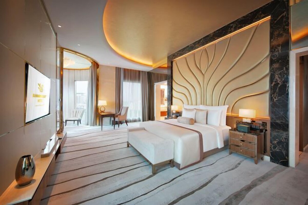 Habitación de hotel con una cama grande, un televisor de pantalla plana, un escritorio con una silla y una zona de estar con mesa y sillas.
