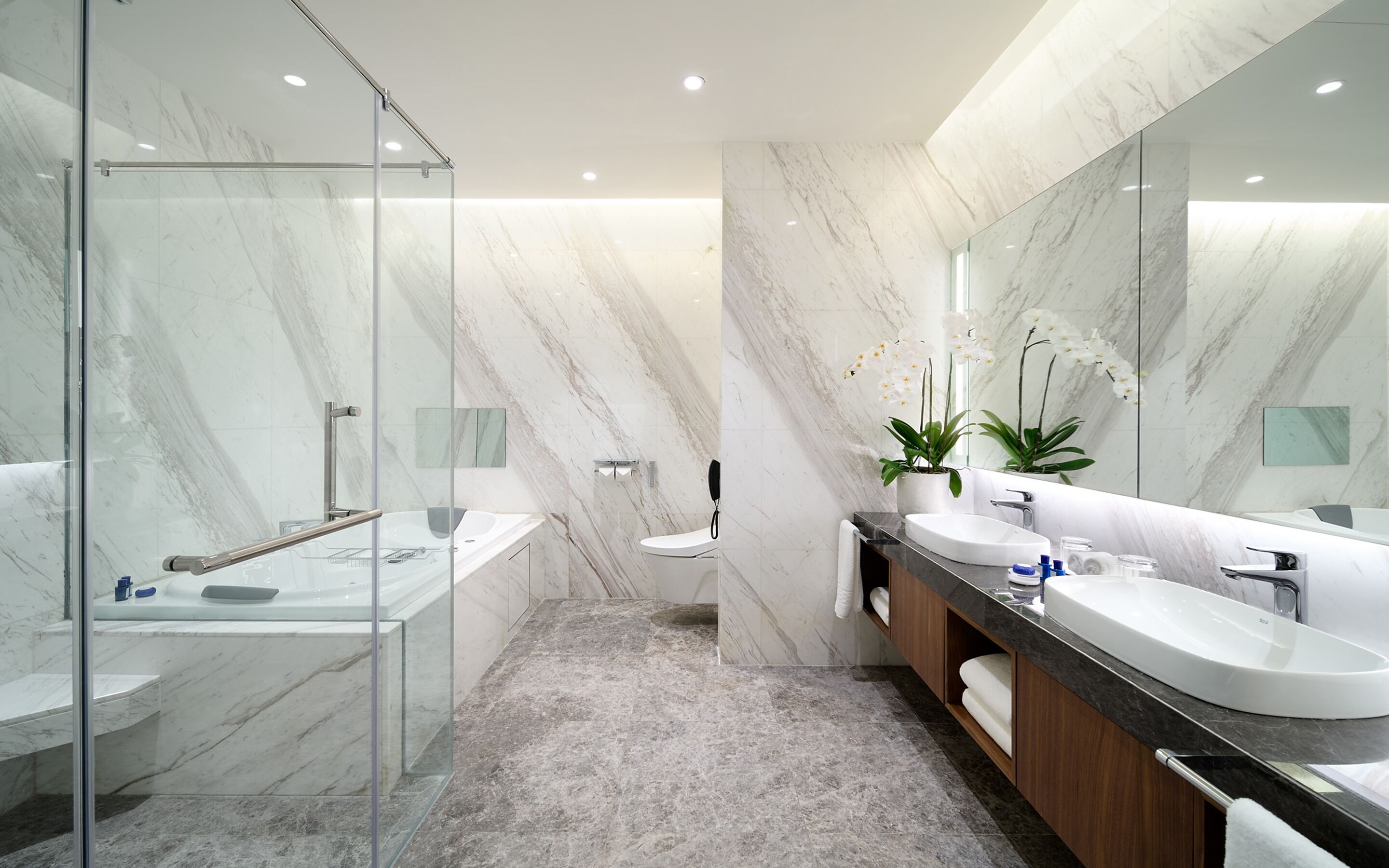 A modern bathroom with a glass shower enclosure, a marble-tiled floor, a white sink, and a large mirror.