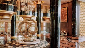 Un lobby lujoso con una escultura de vidrio central, techos altos y candelabros modernos.