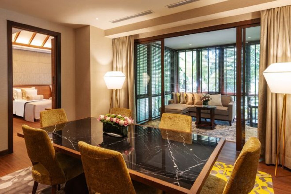 A hotel room with a dining area featuring a marble table, yellow chairs, and a sofa set.