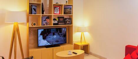 Una sala de estar con televisión, estanterías, un sofá rojo y dos lámparas.