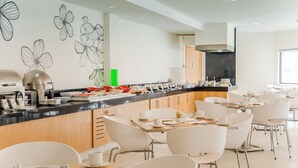 A modern kitchen with a long counter, white chairs, and a wall with black floral designs. - Fiesta Inn Express Monclova (Monclova)