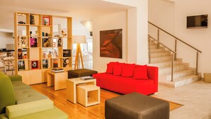 A modern living room with a red sofa, green and black ottomans, a wooden bookshelf, and a staircase. - Fiesta Inn Express Monclova (Monclova)