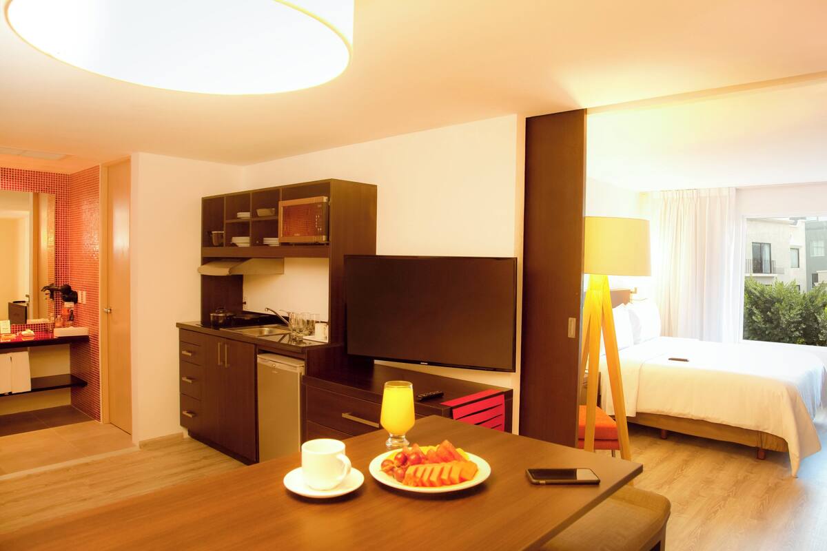Une chambre d’hôtel avec une table à manger dressée pour le petit-déjeuner, une télévision, un lit et une vue sur l’extérieur.