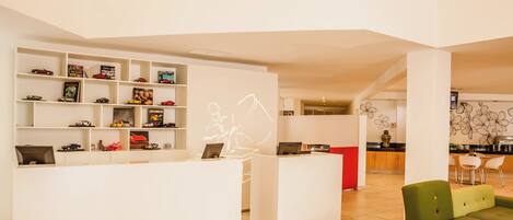 Een moderne receptie met witte bureaus en een groene bank, omringd door planken met diverse spullen.