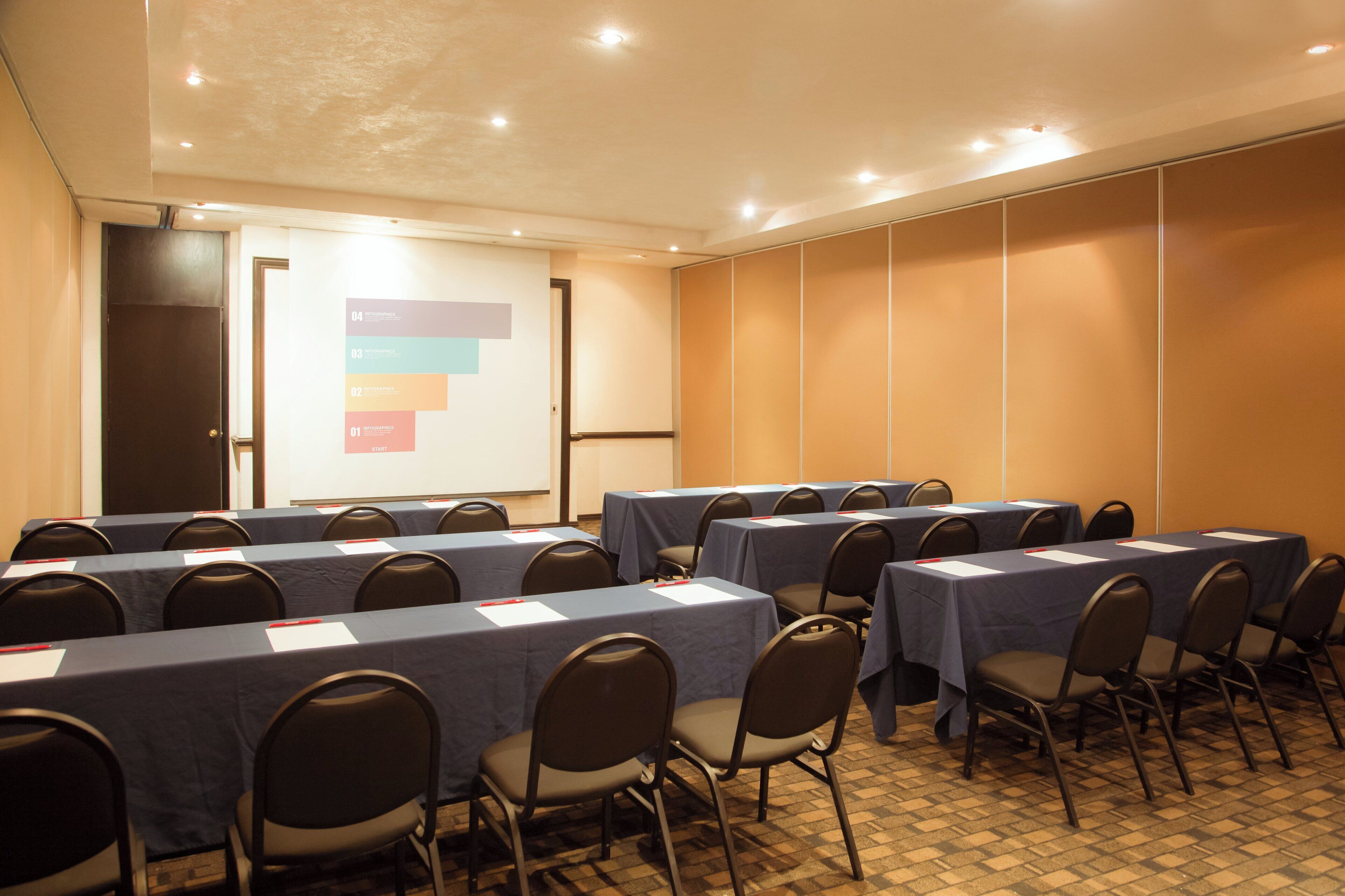 A conference room with multiple tables and chairs, a projector screen, and a presentation on the wall.