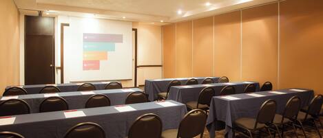 A conference room with multiple tables and chairs, a projector screen, and a presentation on the wall.