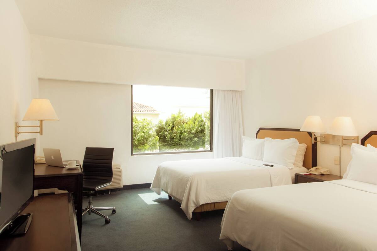 Une chambre d’hôtel avec deux lits, un bureau avec un ordinateur portable, une chaise et une télévision.