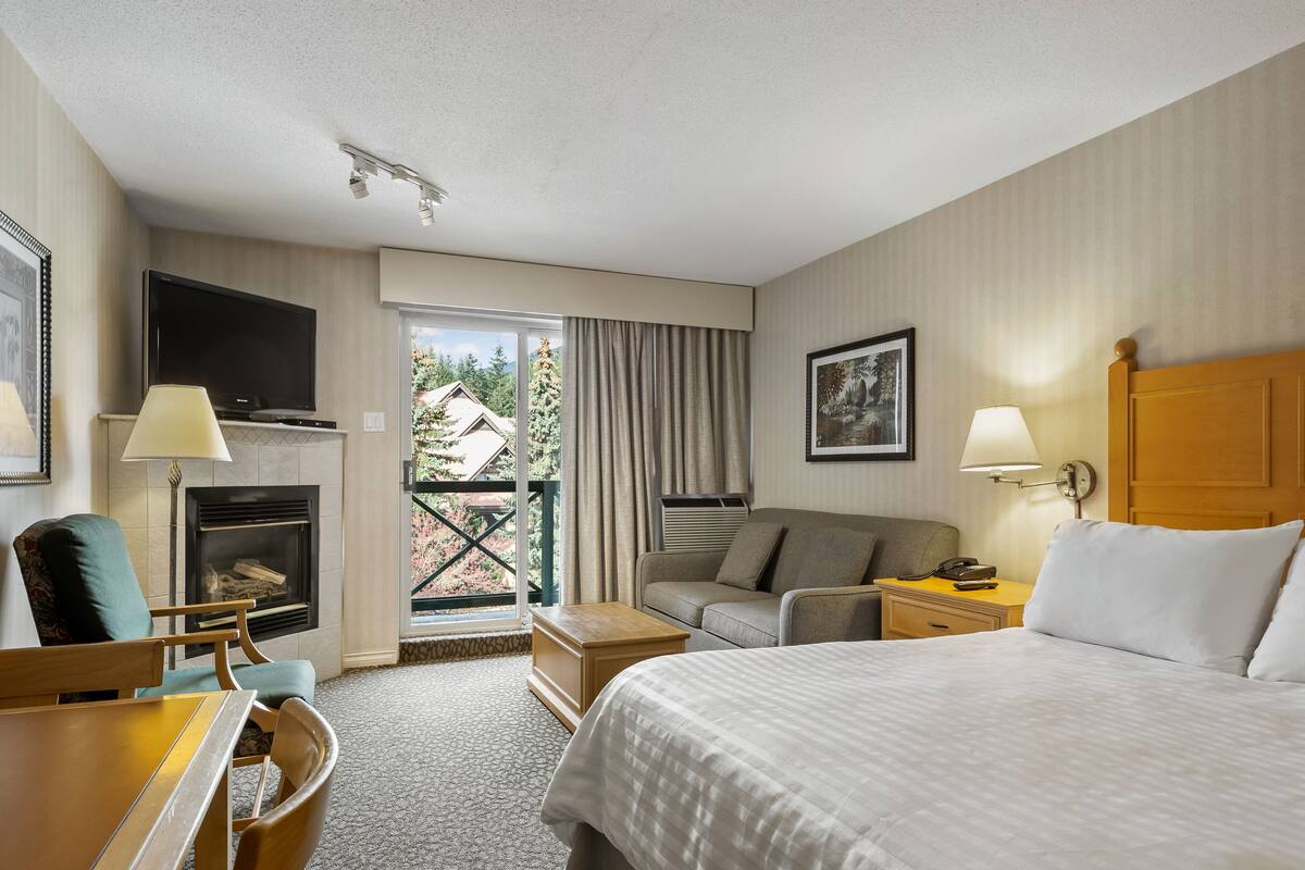 Een hotelkamer met een bed, een bank, een bureau met een lamp, een televisie en een open haard.